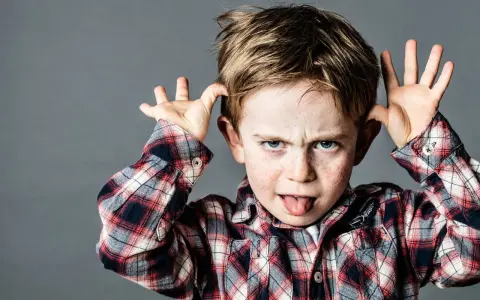 Ein frecher Junge mit Sommersprossen zieht Grimassen und steckt die Zunge heraus, ein Ausdruck dafür, wenn Kinder frech und respektlos sind.