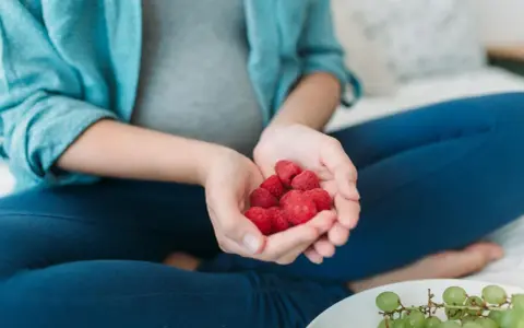 Schwangere Frau hält Himbeeren in den Händen. Die roten Früchte sind ein gesunder Snack während der Schwangerschaft.