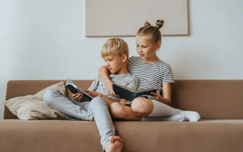 Geschwisterliebe: Ein Mädchen umarmt ihren Bruder, während sie gemeinsam auf dem Sofa lesen. Eine schöne Darstellung ihrer Beziehung.