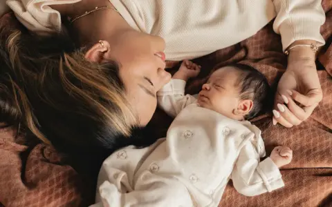 Mutter und Baby liegen eng beieinander. Die Mutter schaut liebevoll auf ihr schlafendes Kind. Ein Moment der Ruhe und Geborgenheit, der die **Baby-Begrenzung beim Schlafen** symbolisiert.