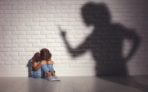 Ein Mädchen kauert weinend auf dem Boden, während ein bedrohlicher Schatten einer erwachsenen Person an der Wand steht. Psychologie: Mutter hasst Tochter?