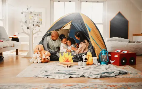 Familie verbringt **gemeinsame Zeit** beim Zelten im Wohnzimmer. Kinder kuscheln mit Teddybären, während Eltern lachen.