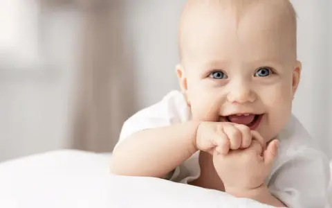 Ein lächelndes Baby mit blauen Augen, das auf einer weißen Decke liegt. Vielleicht ein zukünftiger Träger von langen Jungennamen wie Maximilian oder Alexander.