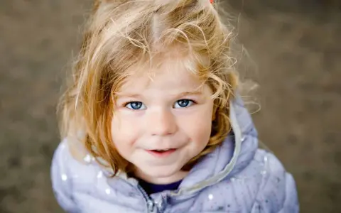 Ein blondes Mädchen mit blauen Augen lächelt. Ihr Haar ist zerzaust, wie bei vielen norddeutschen Frauennamen, die oft eine natürliche Schönheit widerspiegeln.
