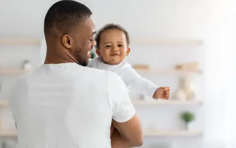 Ein Vater hält sein lächelndes Baby. Vielleicht sucht er nach christlichen Jungennamen für seinen kleinen Schatz.