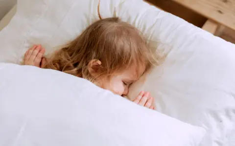 Kleines Kind schläft friedlich im Bett. Ab wann schlafen Kinder alleine ein? Diese süße Szene zeigt einen friedlichen Schlaf.
