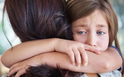 Ein trauriges Kind umarmt seine Mutter. In der Grundschule darf das Kind nicht mitspielen, es fühlt sich ausgeschlossen.