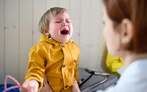 Ein weinendes Kind im Kindergarten, das nach Mama ruft. Die Erzieherin versucht, das kleine Mädchen zu trösten.