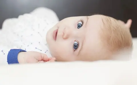 Ein Baby mit strahlend blauen Augen und blonden Haaren, das neugierig in die Kamera blickt. Ein süßer kleiner Kerl, der bestimmt mal einer der freche jungennamen tragen wird.