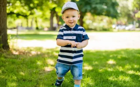 Ein lächelnder Junge mit Kappe und gestreiftem Polo-Shirt im Park. Vielleicht heißt er Finn, Leo oder Noah – beliebte Jungennamen mit 4 Buchstaben.