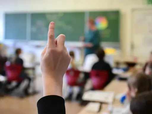 Ein Schüler hebt die Hand, um eine Frage zu stellen. Wie lange muss man in die Schule gehen? Die Antwort liegt im Unterricht.