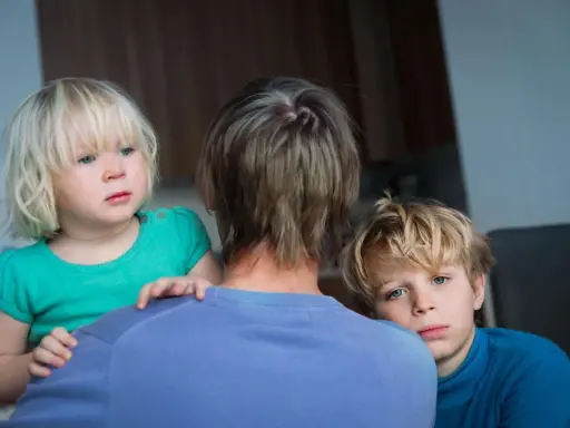 Zwei Kinder blicken besorgt über die Schulter einer Person. Die **Trennung wegen unterschiedlicher Erziehung** scheint sie zu belasten.