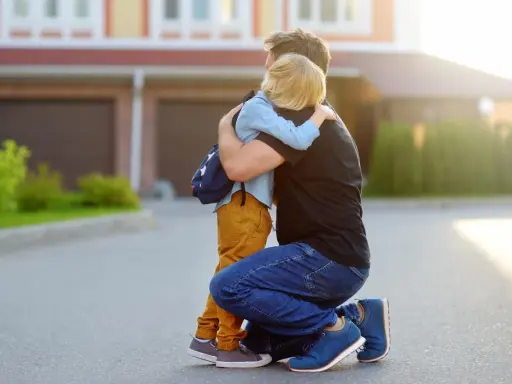 Vater umarmt seinen Sohn mit Rucksack. Ein guter Schulstart nach den Ferien beginnt mit einer liebevollen Umarmung.