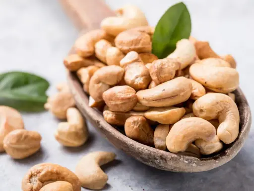 Holzkelle voller Cashewkerne, ideal für die Schwangerschaft. Zwei grüne Blätter liegen daneben.