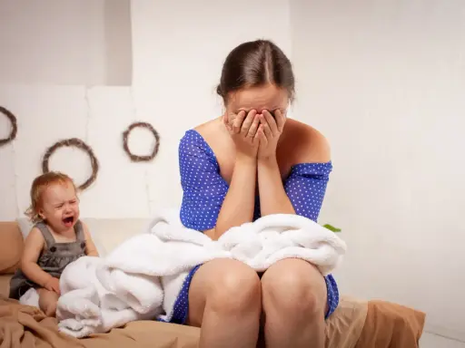 Verzweifelte Mutter mit Baby, das weint. Sie verbirgt ihr Gesicht in den Händen, vielleicht denkt sie: "Regretting motherhood was tun?