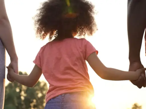 Kind hält Hände von Eltern. Die gesetzliche Regelung Kinderbetreuung Trennung soll das Wohl des Kindes sichern.