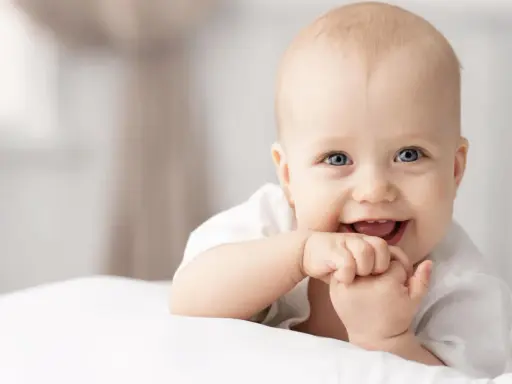 Ein lächelndes Baby mit blauen Augen, das auf einer weißen Decke liegt. Vielleicht ein zukünftiger Max oder Mika, einer der beliebten Jungennamen mit M.