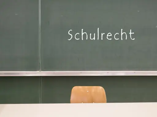 Grüne Tafel mit der Aufschrift "Schulrecht". Ein leerer Stuhl davor. Hier werden die Elternpflichten für Hausaufgaben und das Schulrecht thematisiert.