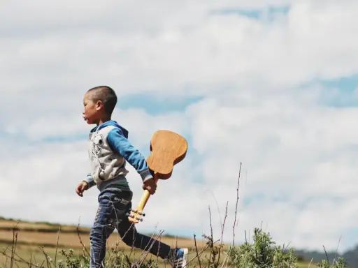 Ein kleiner Junge, vielleicht 18 Monate, rennt mit einer Ukulele durch die Natur. Ein sehr anstrengender, aber glücklicher Moment.