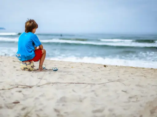 Ein Junge sitzt allein am Strand auf einem Fußball. Er blickt aufs Meer. Meine Tochter 16 hat keine Freunde, sie fühlt sich oft so einsam.