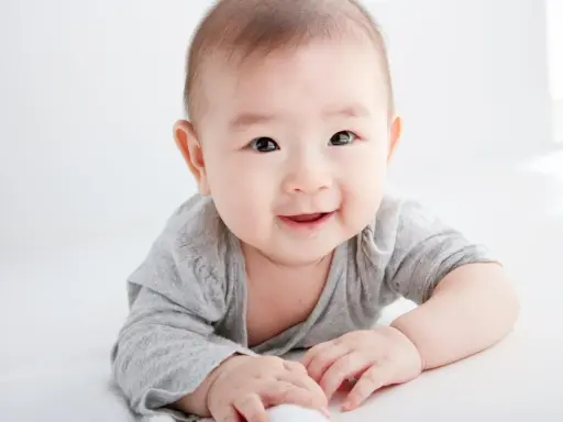 Lächelndes Baby in grauem Shirt auf weißem Hintergrund.