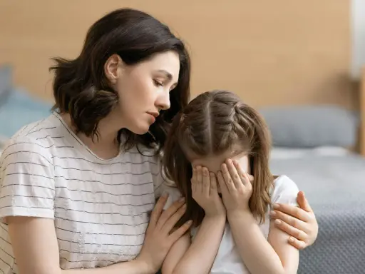 Eine Mutter tröstet ihr weinendes Kind, das sich die Augen zuhält. Möglicherweise kämpft das Kind mit Zwangsgedanken bei Kindern.