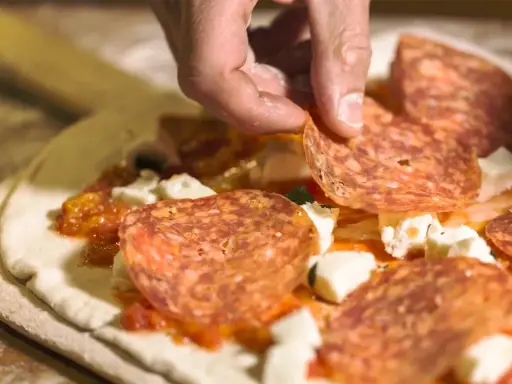 Hand belegt Pizza mit Salami. Frage: darf man in der schwangerschaft salami essen? Die Antwort ist ja, wenn sie gut durchgegart ist.