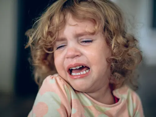 Ein kleines Mädchen mit lockigen Haaren weint bitterlich. Tränen laufen über ihr Gesicht, die Augen sind geschlossen. Ein Ausdruck von starkem **Wut bei Kindern** ist deutlich zu sehen.