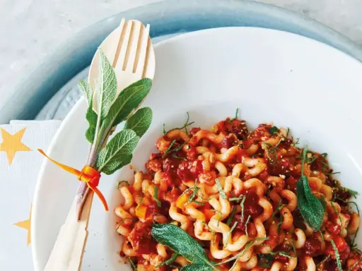 Gedrehte Pasta mit Bolognese-Sauce, garniert mit Salbei. Ein Holzgabel-Set mit Kräutern, passend zur bolognese schwangerschaft.