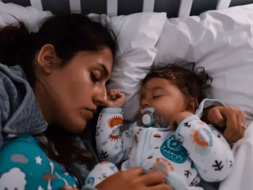 Mutter und Baby schlafen eng aneinander gekuschelt im Bett. Das Baby hat einen Schnuller im Mund. Ein friedlicher Moment, der zeigt, dass man nicht immer alleine ins Bett gehen muss.
