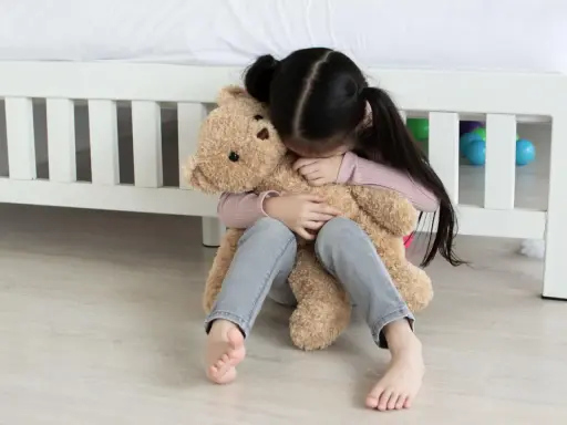 Ein trauriges Kind umarmt seinen Teddybär. Tipps, was tun gegen heimweh kinder, um Trost zu spenden.