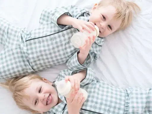 Zwei süße Jungen in karierten Pyjamas trinken aus Fläschchen. Perfekt für Inspiration für Zwillingsnamen Jungen!