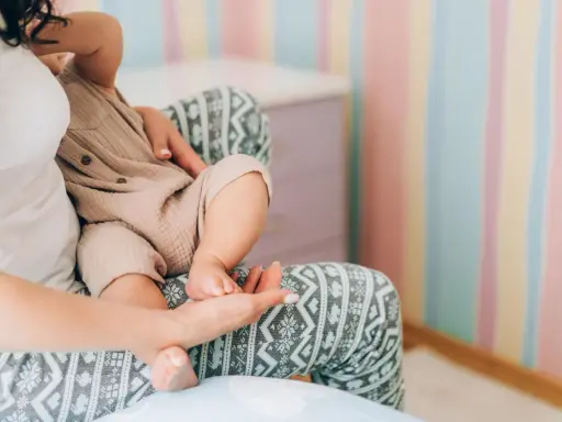 Mutter hält ihr Baby, das auf ihrem Schoß sitzt. Die Streifenwand im Hintergrund ist farbenfroh. Wenn die Mutter während der Stillzeit Durchfall hat, ist das Baby sicher.