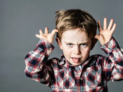 Ein frecher Junge mit Sommersprossen zieht Grimassen und steckt die Zunge heraus, ein Ausdruck dafür, wenn Kinder frech und respektlos sind.