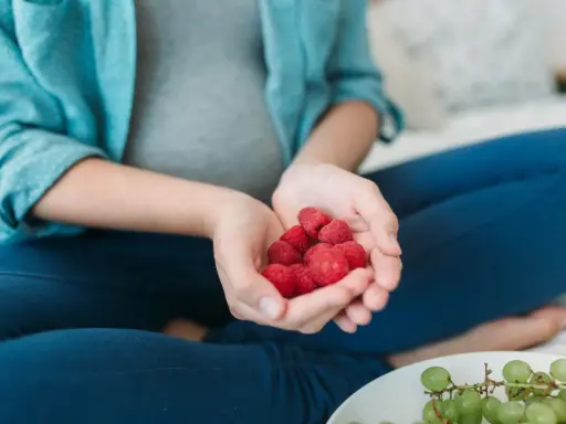 Schwangere Frau hält Himbeeren in den Händen. Die roten Früchte sind ein gesunder Snack während der Schwangerschaft.