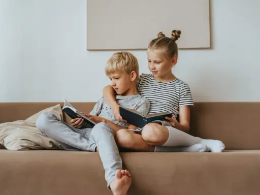 Geschwisterliebe: Ein Mädchen umarmt ihren Bruder, während sie gemeinsam auf dem Sofa lesen. Eine schöne Darstellung ihrer Beziehung.