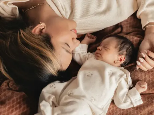 Mutter und Baby liegen eng beieinander. Die Mutter schaut liebevoll auf ihr schlafendes Kind. Ein Moment der Ruhe und Geborgenheit, der die **Baby-Begrenzung beim Schlafen** symbolisiert.