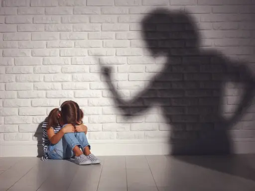 Ein Mädchen kauert weinend auf dem Boden, während ein bedrohlicher Schatten einer erwachsenen Person an der Wand steht. Psychologie: Mutter hasst Tochter?