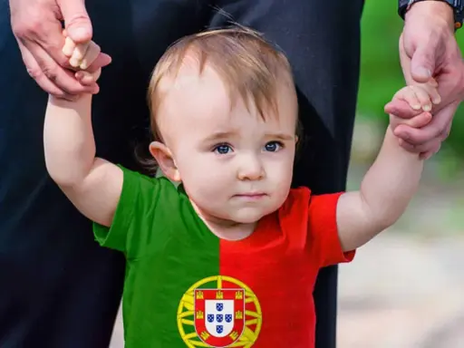 Ein süßes Baby mit portugiesischer Flagge auf dem T-Shirt, gehalten von einer Hand. Vielleicht ein zukünftiger João oder Miguel, inspiriert von portugiesischen Jungennamen.