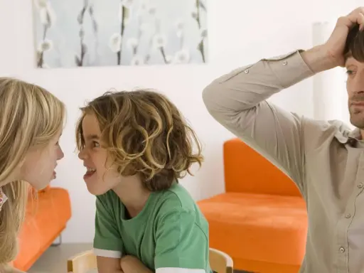 Zwei Kinder streiten sich heftig, während der Vater verzweifelt die Hände über dem Kopf zusammenschlägt. Ein Bild von Geschwisterhass und möglichen Erziehungsfehlern.