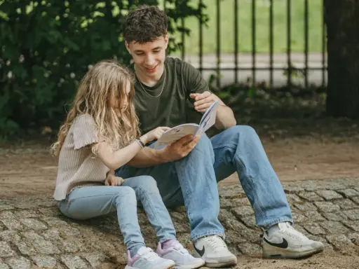 Ein junger Mann liest einem Mädchen im Park vor. Trotz der Trennung der Eltern finden die Kinder Trost und Nähe in gemeinsamen Momenten.