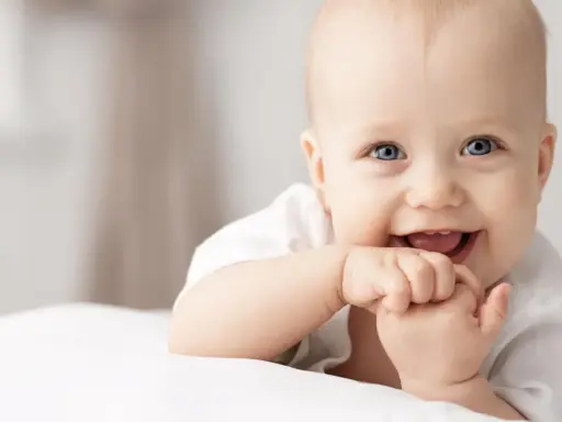 Ein lächelndes Baby mit blauen Augen, das auf einer weißen Decke liegt. Vielleicht ein zukünftiger Träger von langen Jungennamen wie Maximilian oder Alexander.