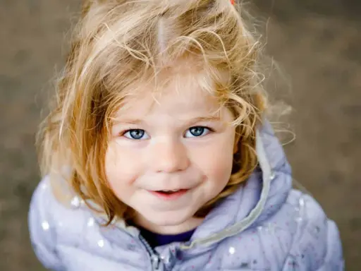 Ein blondes Mädchen mit blauen Augen lächelt. Ihr Haar ist zerzaust, wie bei vielen norddeutschen Frauennamen, die oft eine natürliche Schönheit widerspiegeln.