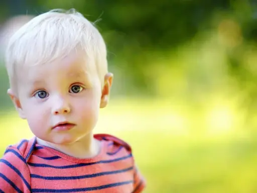 Ein kleiner Junge mit blonden Haaren und blauen Augen blickt neugierig in die Kamera. Sein gestreiftes Shirt erinnert an die Vielfalt von Jungennamen international.