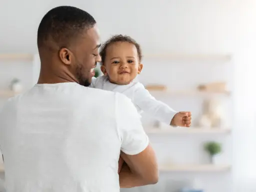 Ein Vater hält sein lächelndes Baby. Vielleicht sucht er nach christlichen Jungennamen für seinen kleinen Schatz.