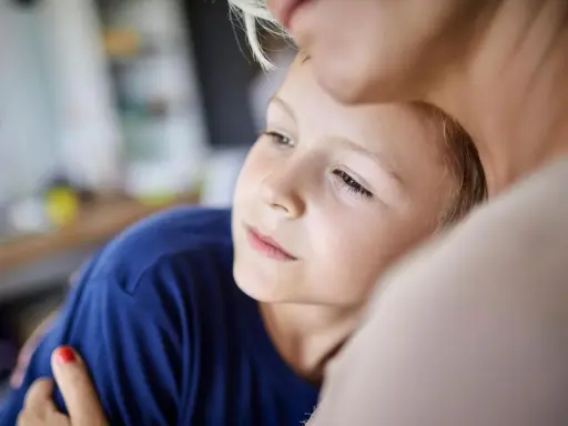 Ein Junge kuschelt sich an eine Frau. Er wirkt nachdenklich, als ob er in ihr eine Art kind als partnerersatz gefunden hätte, der ihm Trost spendet.