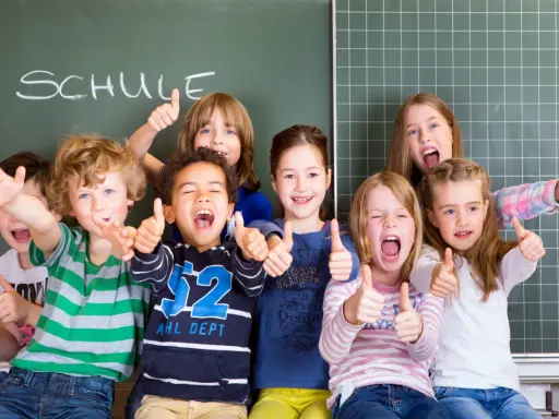 Fröhliche Kinder mit Daumen hoch vor einer Tafel mit dem Wort "SCHULE". Ein perfekter erster schultag!