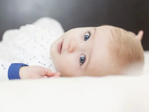 Ein Baby mit strahlend blauen Augen und blonden Haaren, das neugierig in die Kamera blickt. Ein süßer kleiner Kerl, der bestimmt mal einer der freche jungennamen tragen wird.