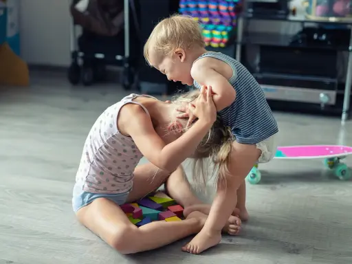 Ein aggressives Kind hält das Haar eines anderen Kindes, das auf bunten Holzklötzen sitzt.