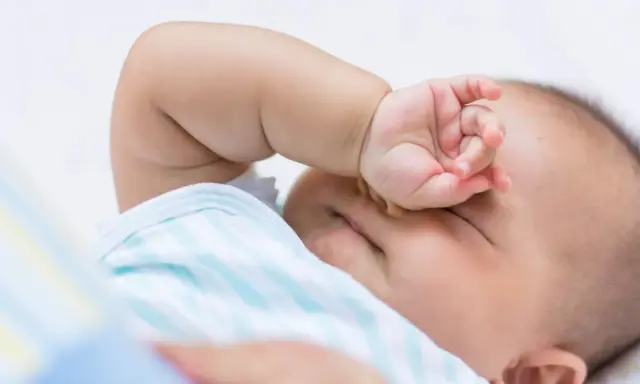 Baby im REM-Schlaf, die Hand vor den Augen, träumt süß.